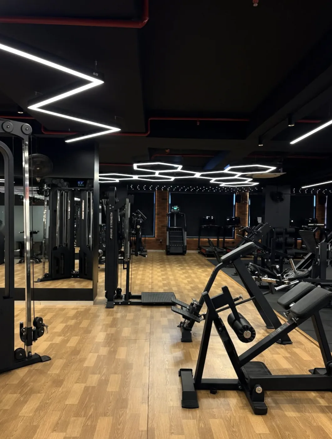 Training floor at Jaguar Fitness Den with hexagon ceiling lights, a cable machine and wooden flooring