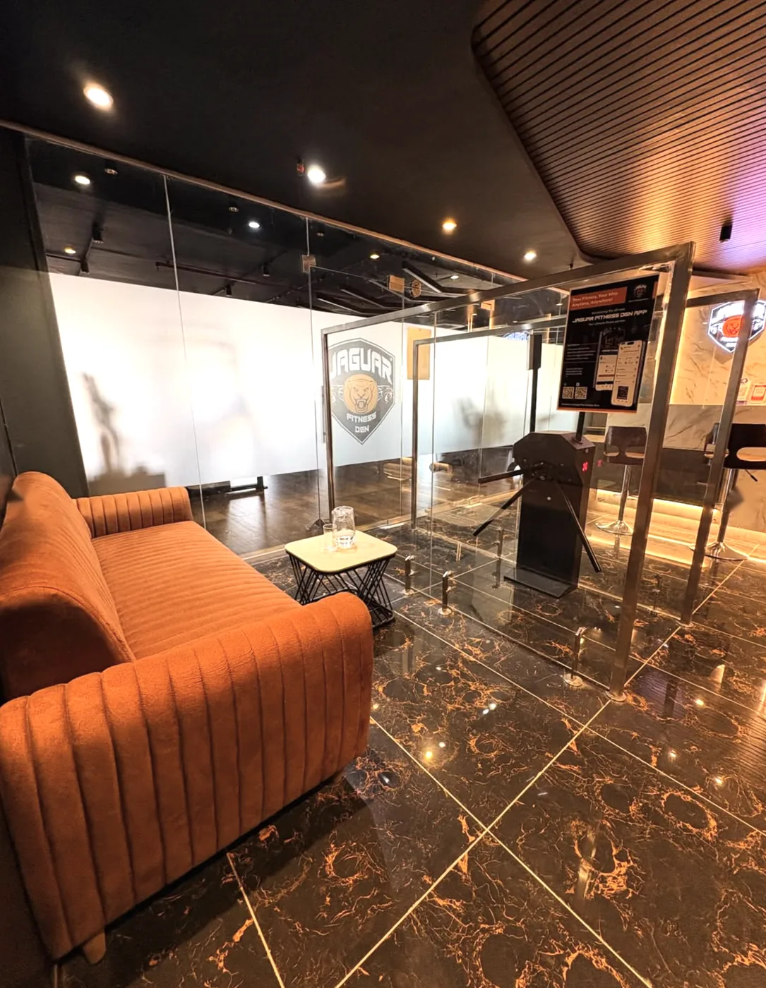 Glass entrance, turnstile and orange sofa at Jaguar Fitness Den